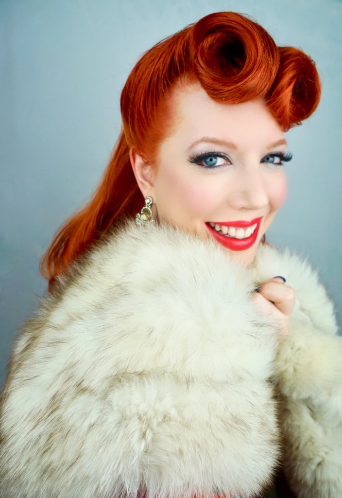 Photo of Renee Nicole Gray smiling with victory rolls in a vintage white fur stole 